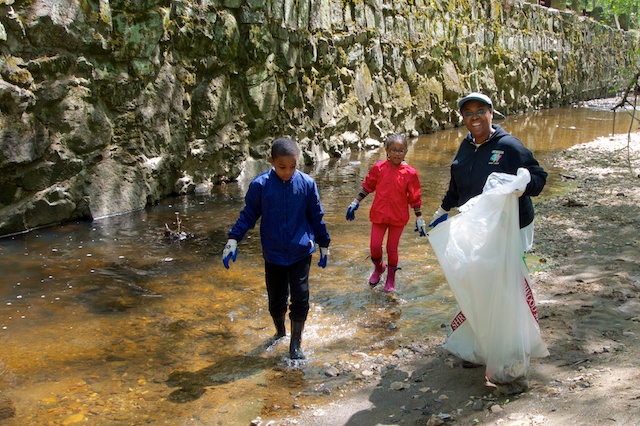 A Dad and two kids sweeping the creek of litter.