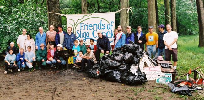 A group of early Sweepers after Sweeping the Creek standing by a FOSC homemade sign and a pile of trash bags.