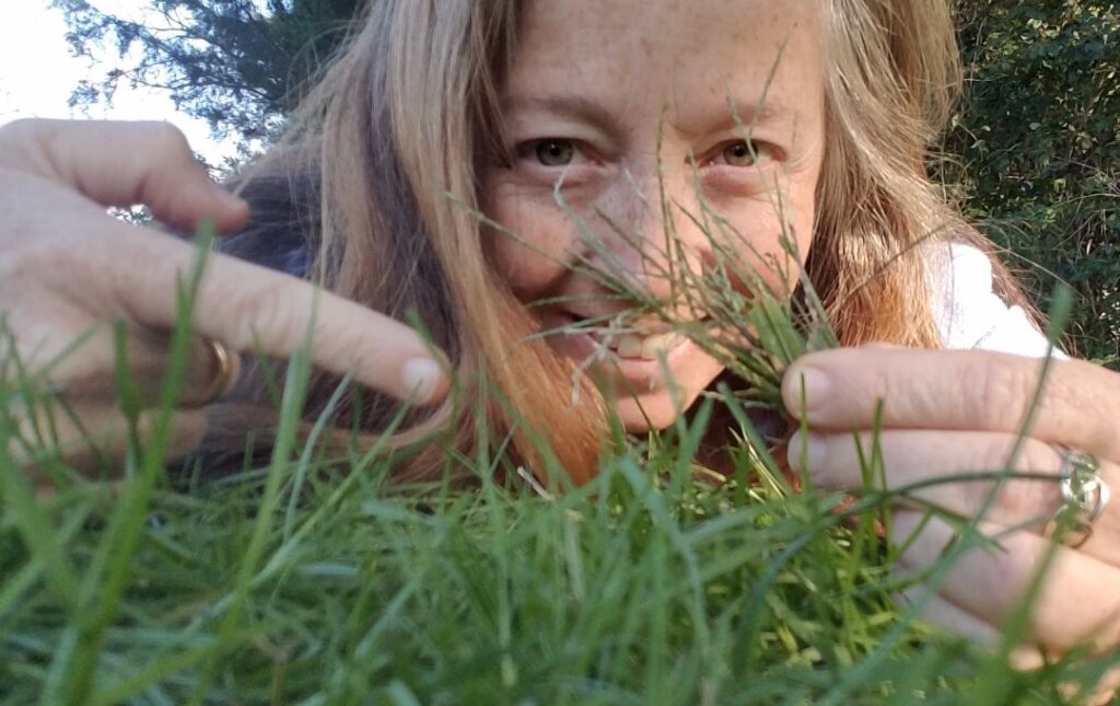 An ant's-eye view of a lawn with a woman holding some grass blades in the background.