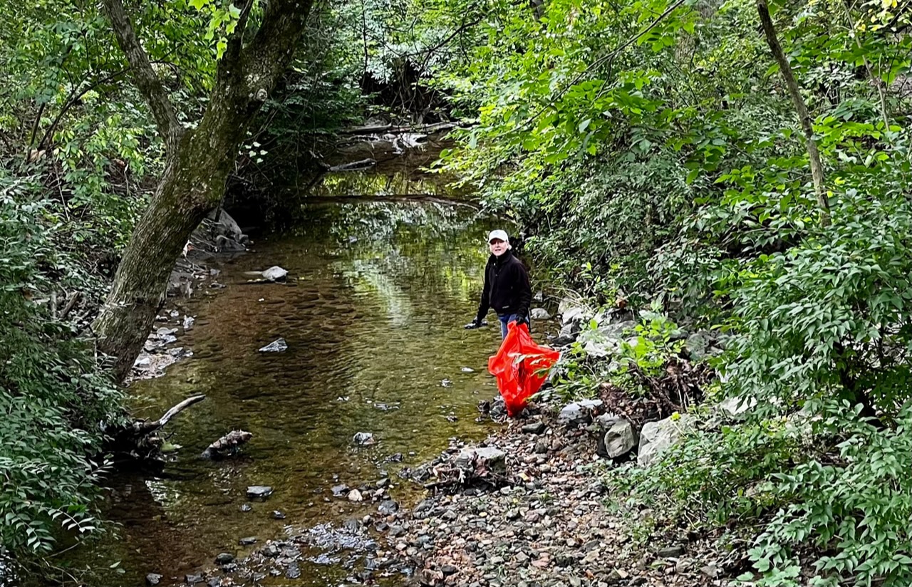 A man with a bottle he removed from the creek to put in the orange trash bag.