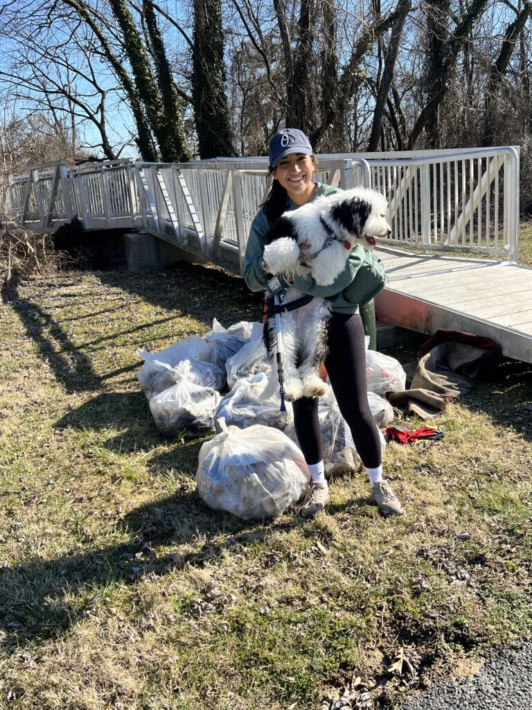 Smiling woman holding her dog next to the trash bags she filled with litter at the Section 1 Sweep.