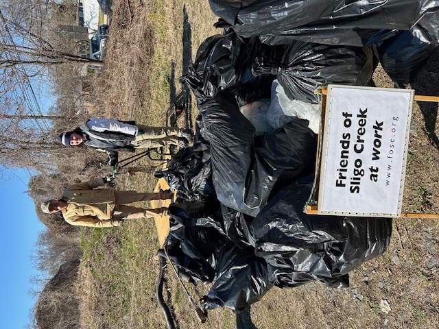Two volunteers surveying the many trash bags and pile of bulky items retrieved from the Wheaton stormwater ponds during the President's Day cleanup