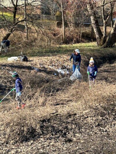People sweeping the Wheaton stormwater ponds of litter amid the brush.